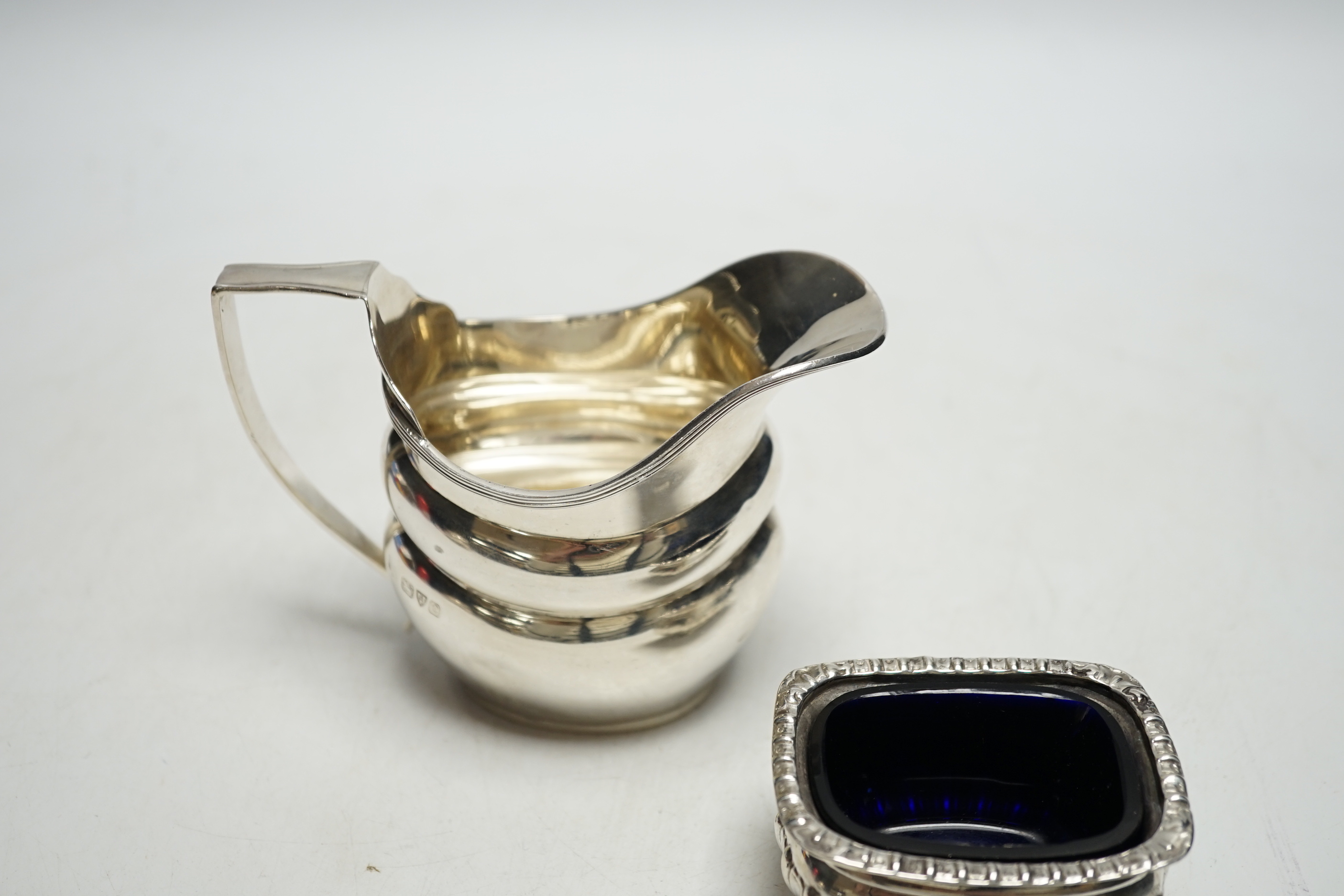 A George V silver helmet shaped cream jug and a silver salt with a gadrooned border.